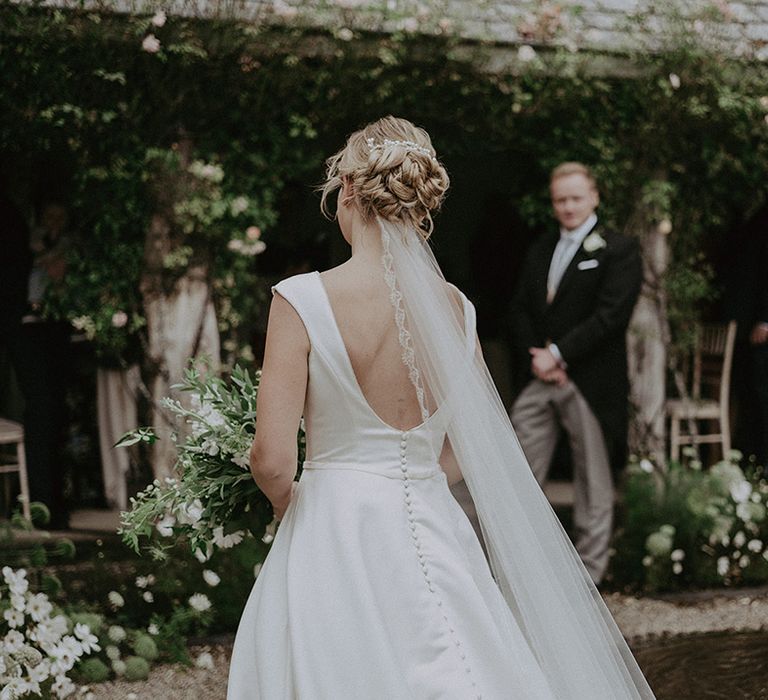 The bride in a San Patrick wedding dress walks down the aisle wearing an embroidered veil with the groom in navy suit 