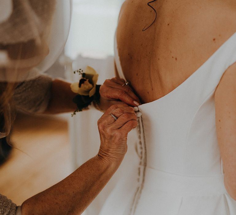 The mother of the bride helps the bride into her button back wedding dress 