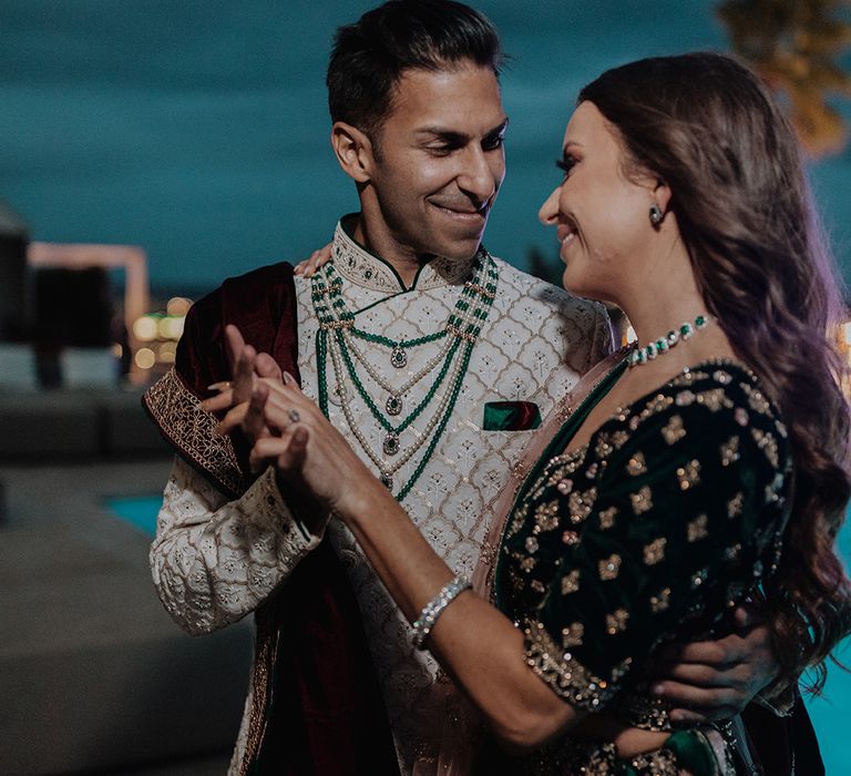 Bride in two piece black and gold patterned saree dancing with groom in white and gold patterned sherwani by the pool at castle wedding venue in Barcelona 