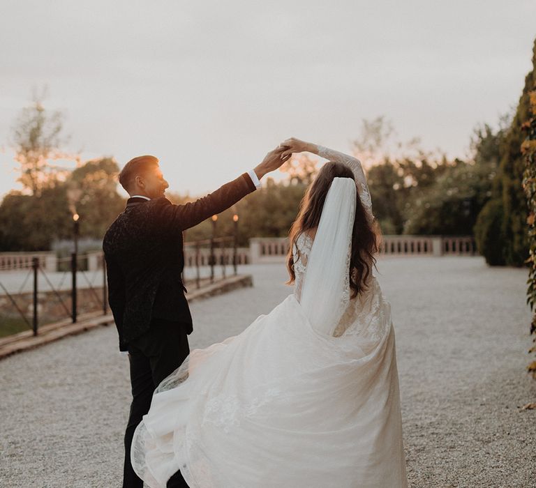 Groom in classic black tux spinning bride around wearing lace long sleeve Pronovias wedding dress and church-length veil