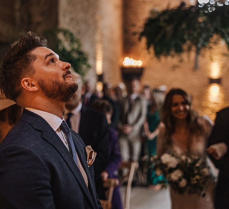 The groom looks up to the sky as he holds in his tears after seeing the bride for the first time walking down the aisle 