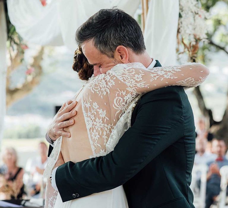 bride in along sleeve lace dress embracing her groom at the altar 