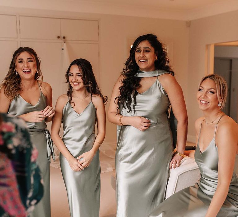 Bridesmaids in satin green mismatched bridesmaid dresses get their first look at the bride in her wedding dress 