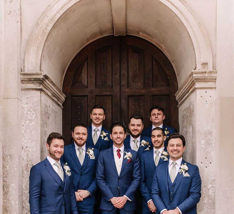 Groomsmen in blue wedding suits with green ties and pocket squares with the groom in matching suit with red tie and pocket square 