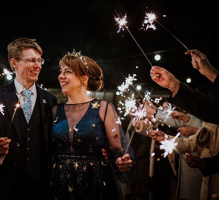 The bride and groom walk out to their guests waving sparklers 