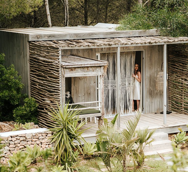 bride in a satin slip peeking through macrame curtain at pure house ibiza wedding venue