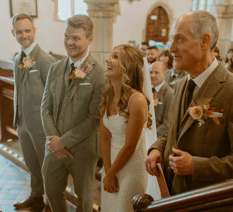 Bride in lace wedding dress with groom in grey suit at their church wedding ceremony 