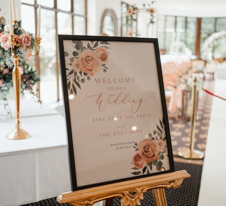 Botanical wedding sign in black rimmed photo frame on gold easel at Bron Eifion wedding venue