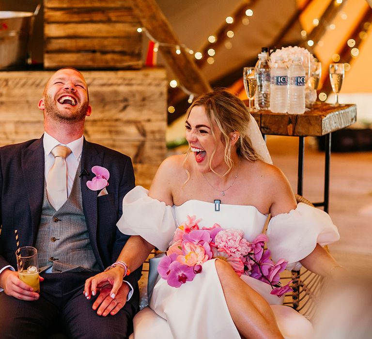 Groom in navy wedding suit with the bride in a Jesus Peiro wedding dress with pink bouquet laughing together 