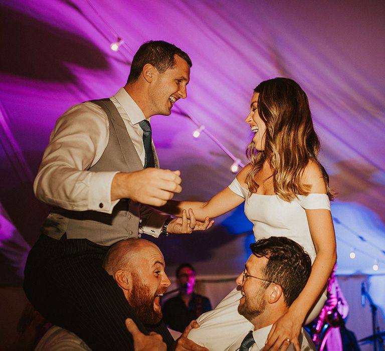 The bride and groom are on the wedding guest's shoulders as they dance together at the wedding reception 