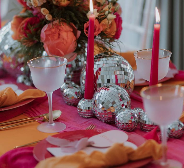 Pink and orange wedding tablescape with bright pink wedding tablecloth, orange wedding napkins, pink tapered candles, pink and orange poppies, garden roses, carnations, dried flowers and foliage wedding table centrepieces and disco ball wedding decor 