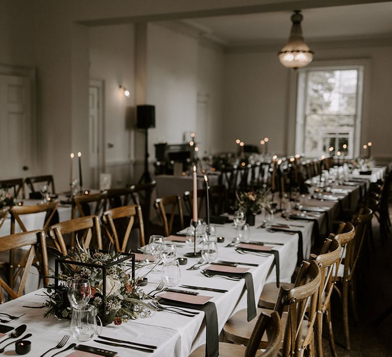 Pink and black taper candles, black napkins and place names, pink place settings, square wedding flower arrangements on the table 