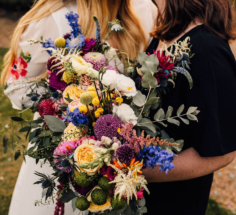 Colourful wildflower wedding bouquet with pink, purple, and yellow flowers held by two brides 