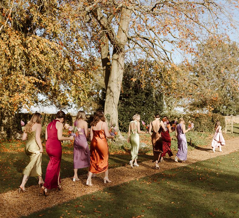 Bridal party wearing mismatched satin bridesmaid dresses in pastel colours walking to the ceremony 