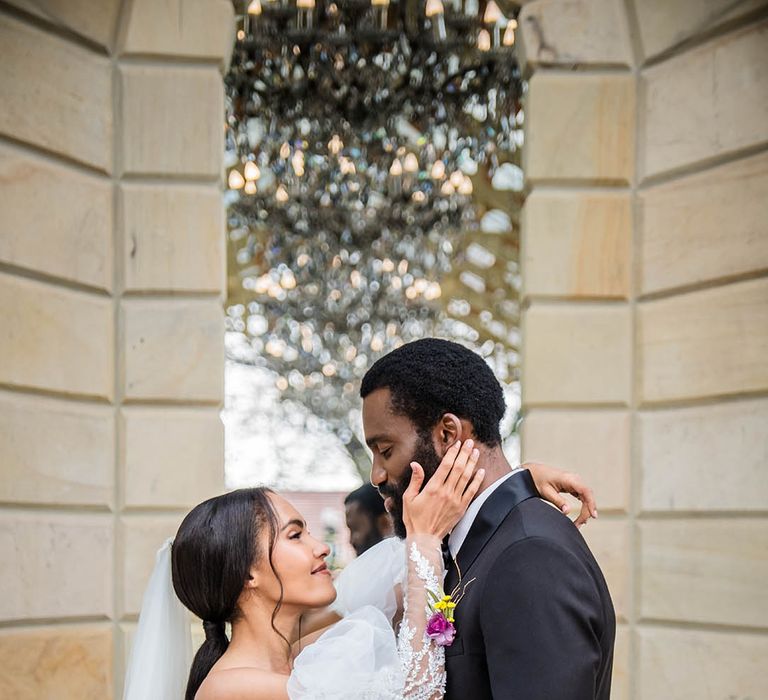 Bride in Milla Nova wedding dress reaches up to groom in black tuxedo 