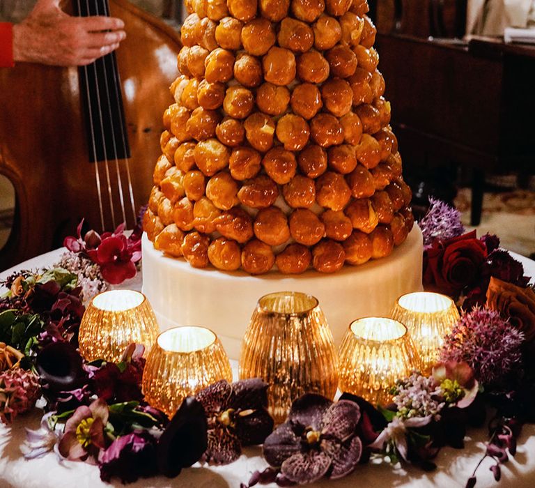 Croquembouche wedding cake alternative surrounded by deep purple and red flowers and candles 