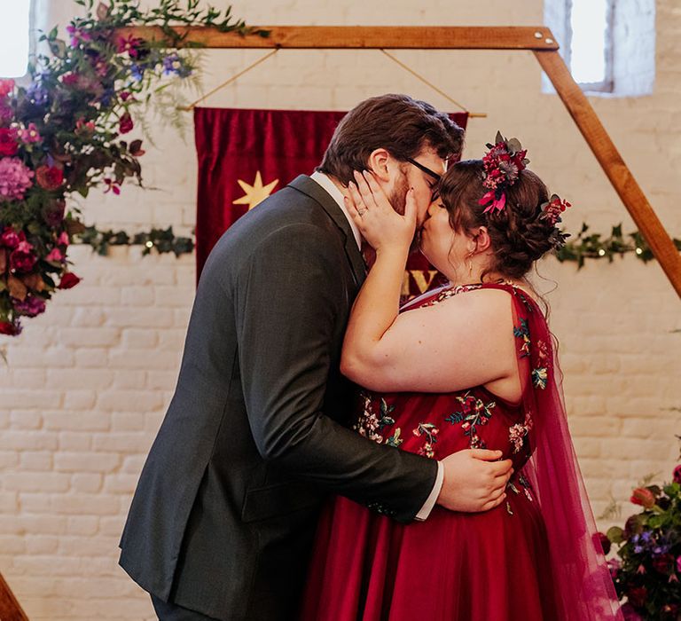 The bride and groom share a kiss to complete the ceremony in front of hexagonal altar decoration and red banner sign 