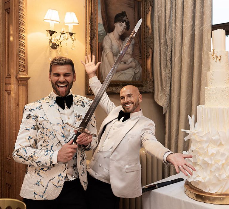 The two grooms cut their luxury all-white seven tier wedding cake together with a sword 