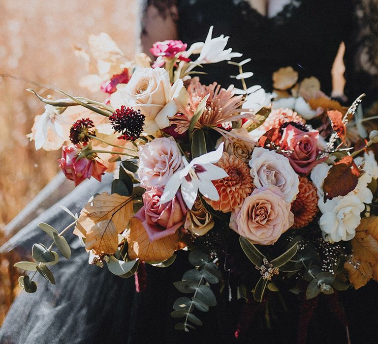 Pink and yellow autumnal wedding bouquet with roses and dahlias decorated with seasonal autumnal leaves 