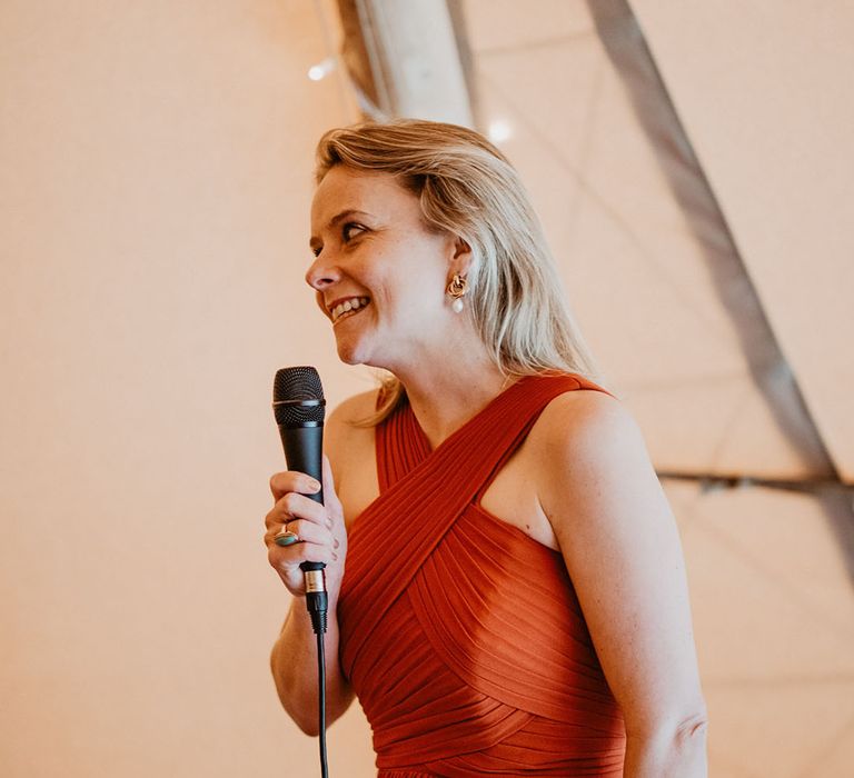 Maid of honour in a burnt orange bridesmaid dress reading out wedding speech 