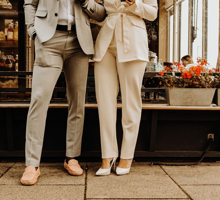 Groom in grey suit and pink loafers and bride in Ivory trouser suit and pumps