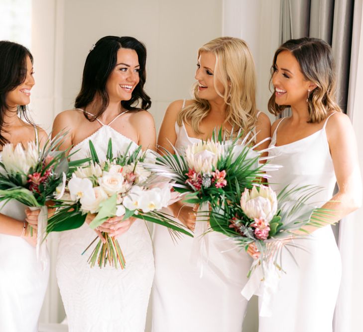 White bridal and bridesmaid dresses with bridal party holding King Protrea wedding flowers