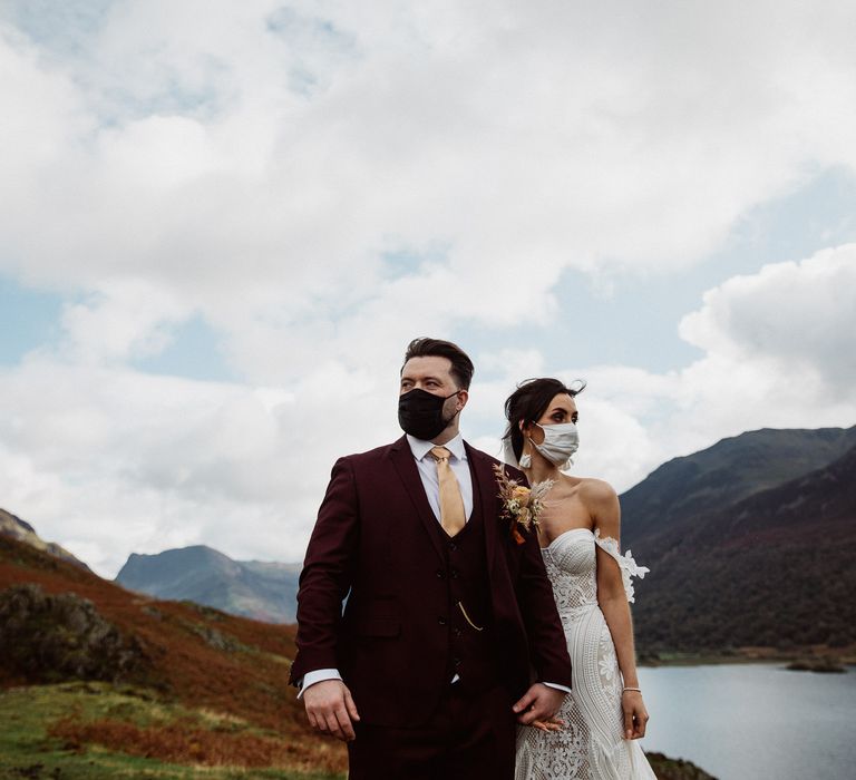 Bride and groom wearing face masks hold hands in the Lake District