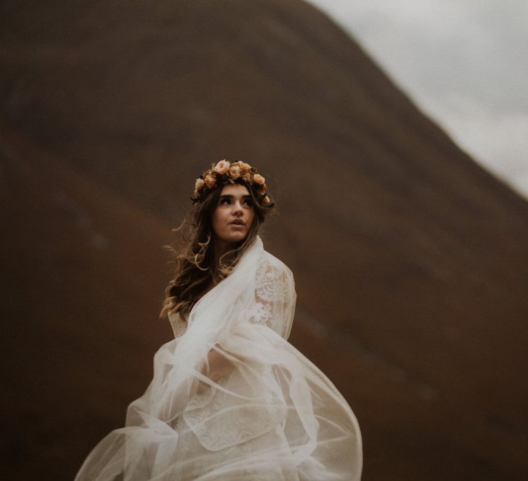 Boho bride in pink rose flower crown with veil blowing in the wind in the Scottish highlands