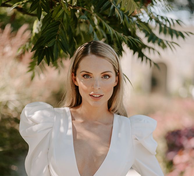 Bridesmaid in white jumpsuit with plunging neckline, puff shoulder and long sleeves