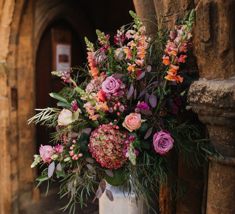 Large bouquet of pink and purple florals line the entrance to the church