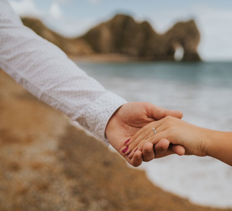 Bride and groom to be holding hands at Durdle door for engagement shoot in Dorset