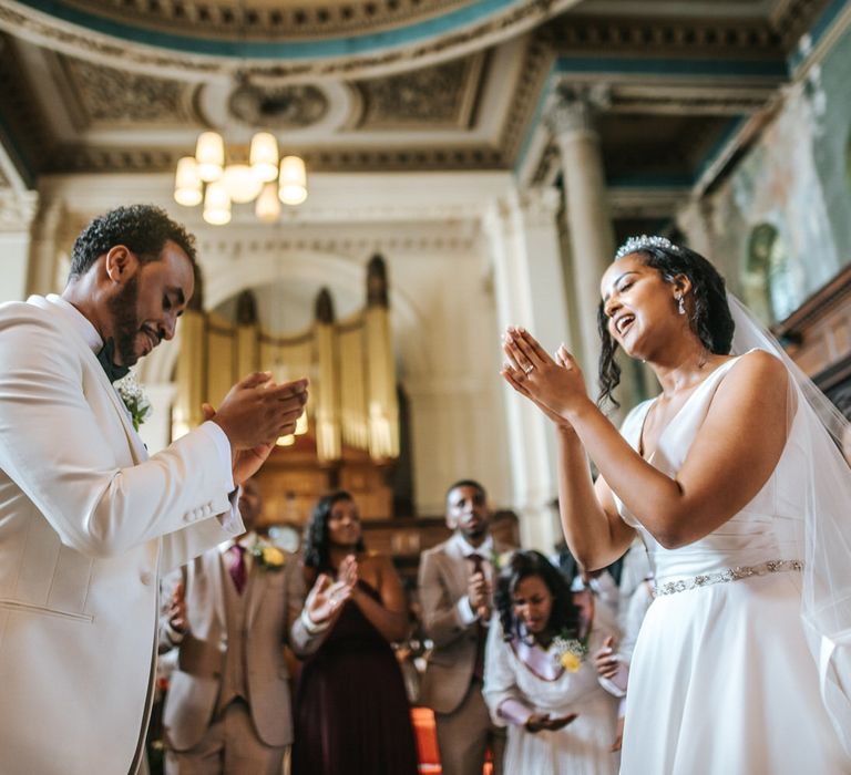 Princess bride and groom in a white tuxedo jacket clapping at Christian wedding ceremony 