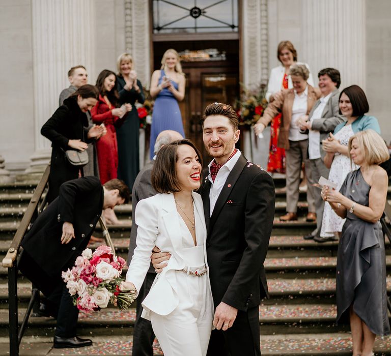 Bride & groom stand in front of steps as wedding party celebrates behind them