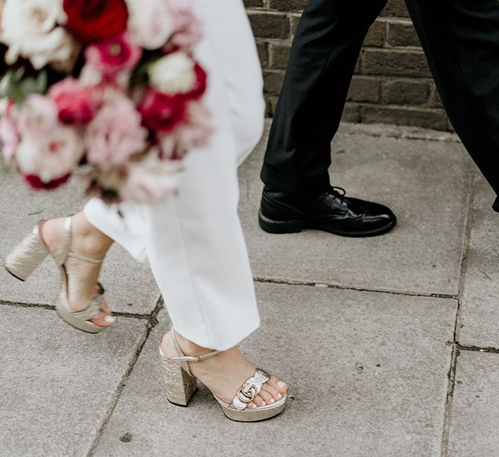 White bridal jumpsuit with Gucci high heels and red floral bouquet 