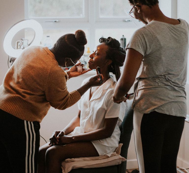 Bride in rollers and white bridal pyjamas gets her make up and hair done before Bridge Community Church Wedding