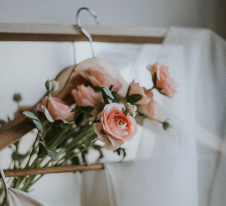 Pink roses threaded through wooden hanger holding white customised satin Bec + Bridge wedding dress