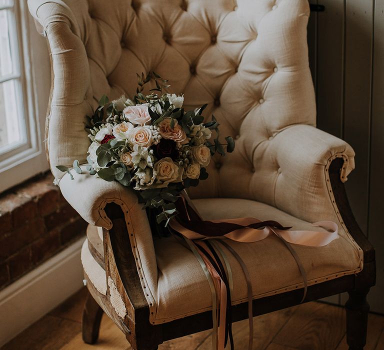 A bouquet of roses and brunia berries and eucalyptus lies on a neutral colour chair. 