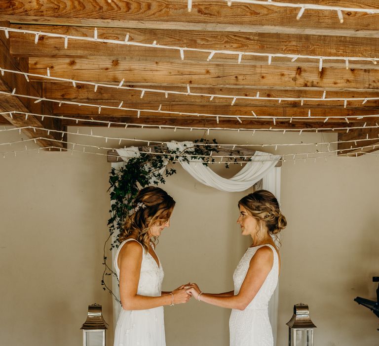 Brides wear boho chic gowns during wedding ceremony whilst holding hands