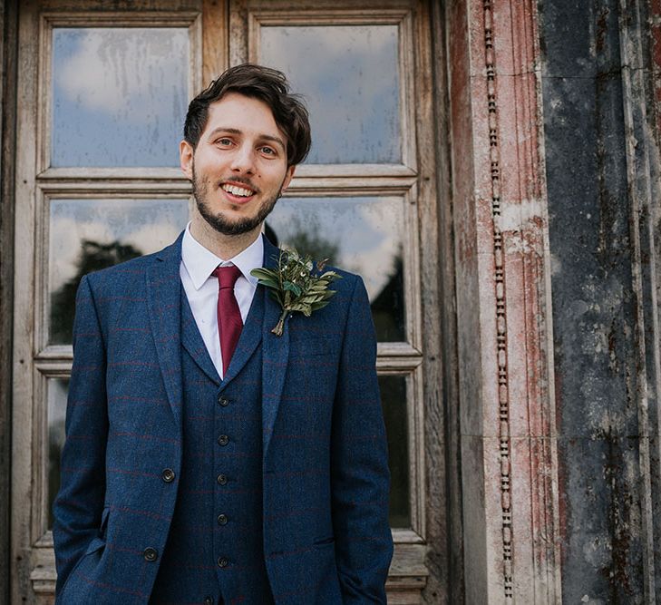 Stylish groom in a navy and red check three-piece wool suit with satin tie and foliage buttonhole 