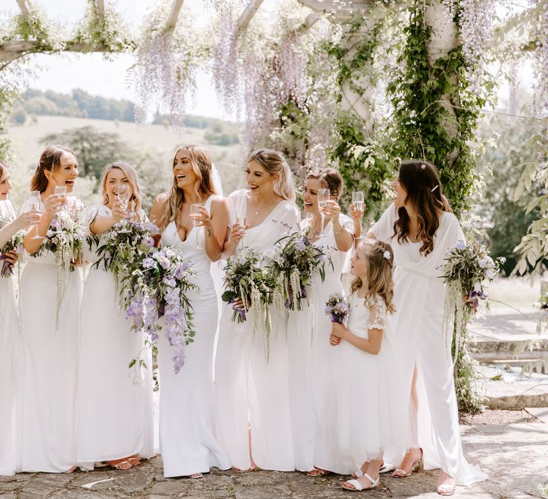 Bride stands with her bridesmaids in white dresses from ASOS all carrying lilac bouquets