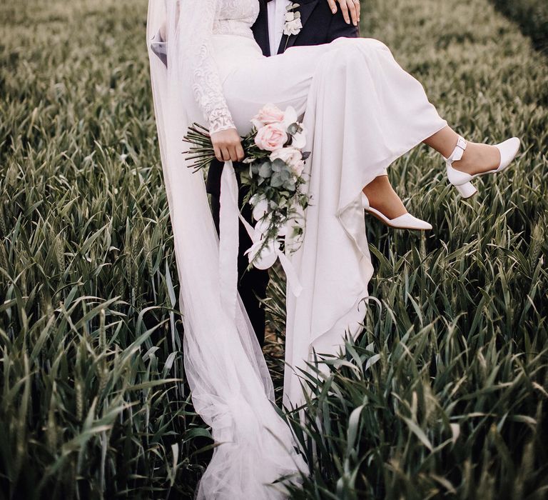 Groom carries his bride through a field with bridal hijab and stunning orchid and rose wedding bouquet