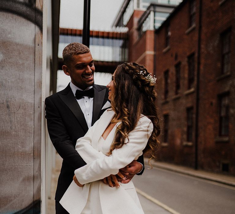 Groom in a black tuxedo embracing his bride in a white suit on the streets in Sheffield 