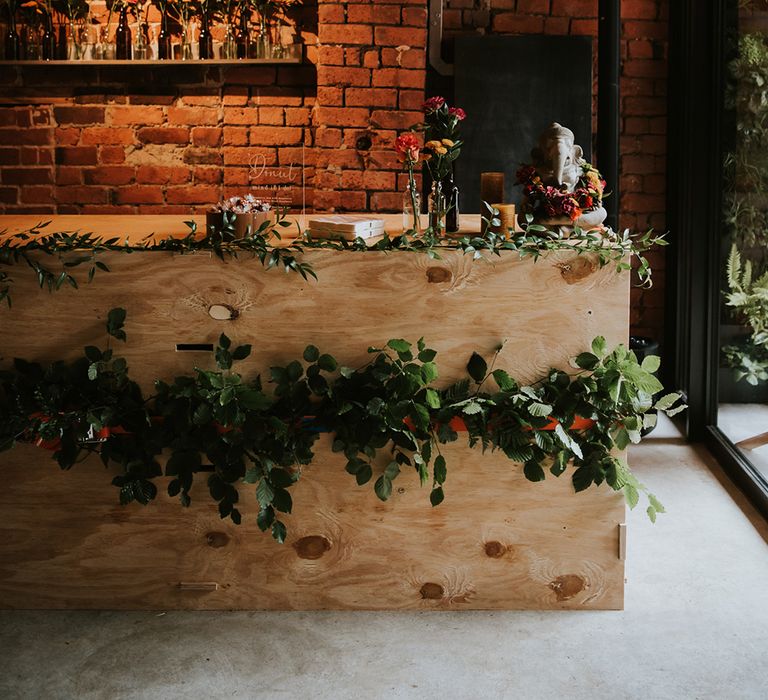 A wooden bar is decorated with flowers at a wedding reception.