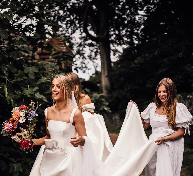 Bridesmaids in white dresses carry bride's dress