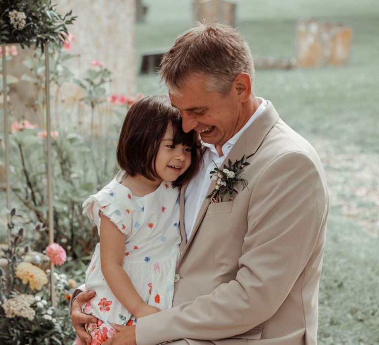 Groomsman in linen suits kneels down with young wedding guest in colourful dress before Wasing Park wedding