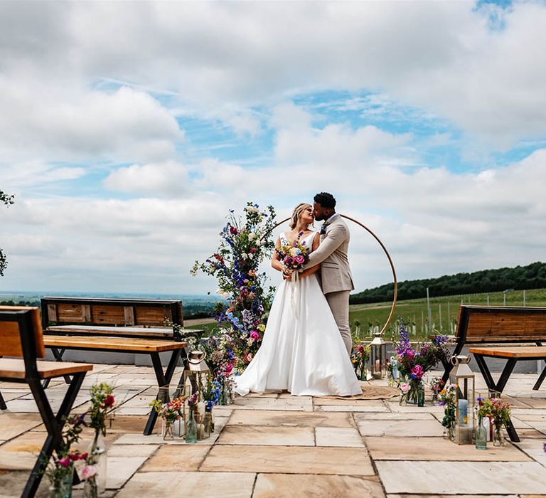 Outdoor wedding at Little Wld Vineyard with wildflowers lining the aisle and a copper hoop altar decorated in colourful flowers 