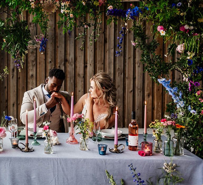 Bride and groom sitting at a sweetheart table decorated with colourful flower stems in vases 