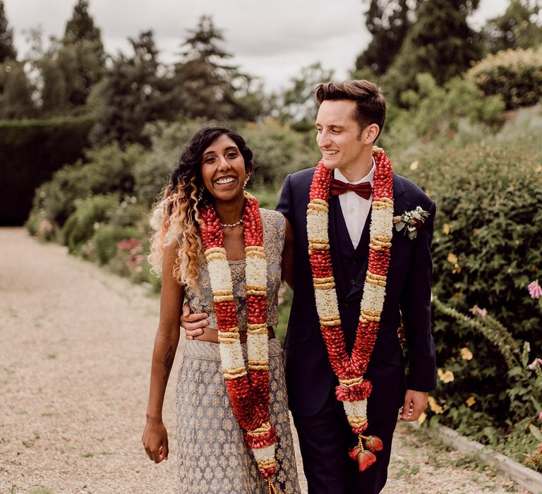 Bride & groom walk together as they have colourful garlands around their necks | Joshua Gooding Photography