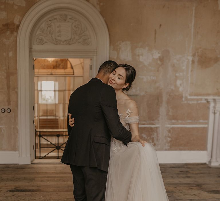 Bride in a tulle wedding dress with illusion neckline dancing with her groom in a black tuxedo in the reception room at Clerkenwell House