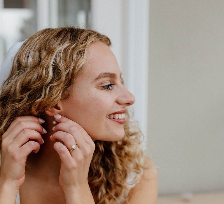 Curly haired bride adds earrings to her bridal look on the morning of her wedding day